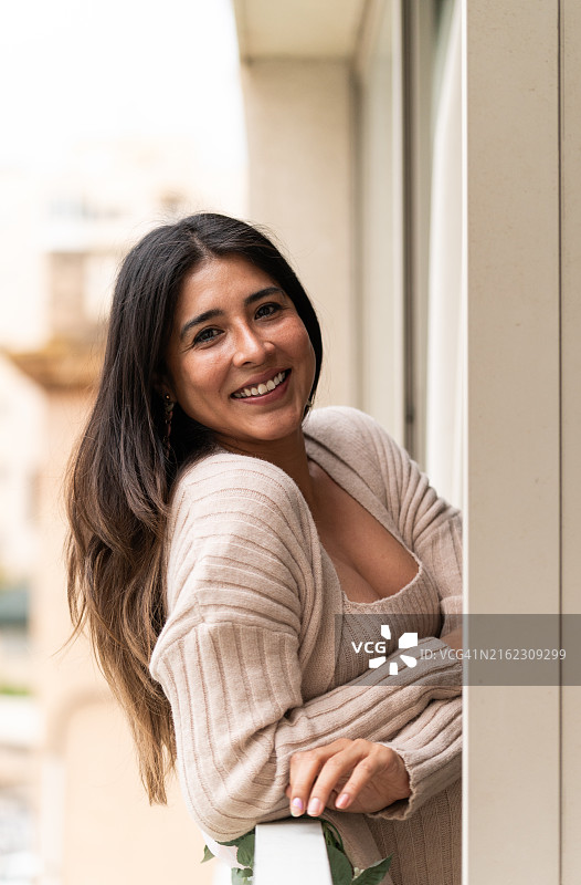 靠在阳台栏杆上微笑的漂亮拉丁女人图片素材