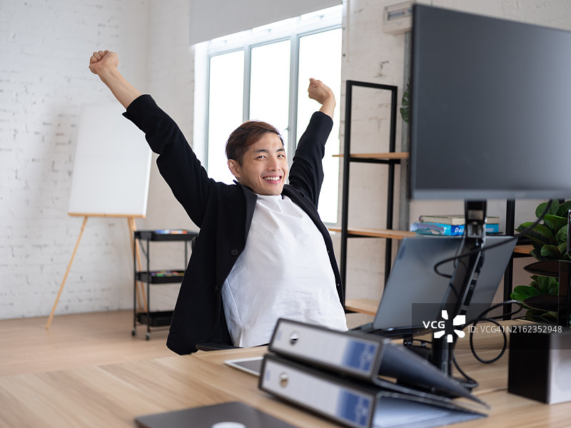 年轻的专业人士在现代办公环境中工作时伸展和打哈欠，表示疲劳或休息图片素材