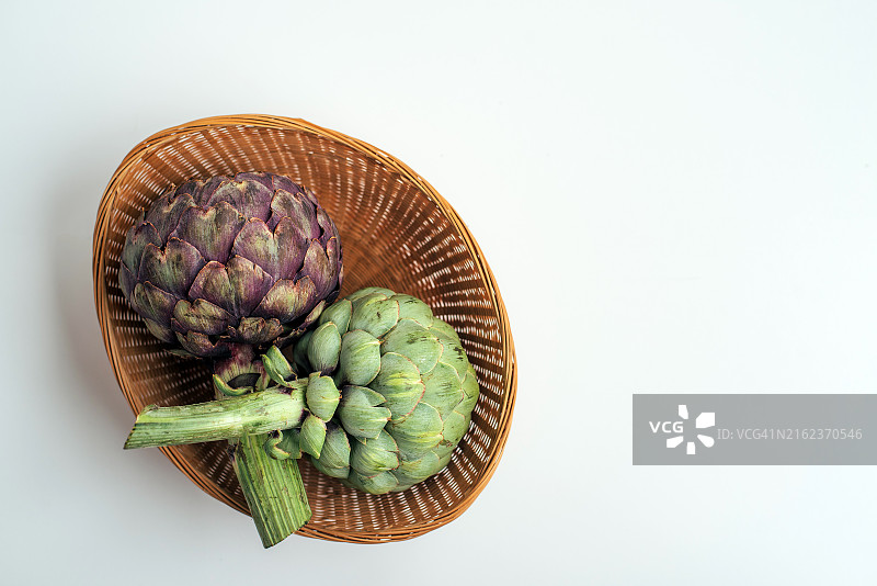 柳条筐里的绿色和紫色朝鲜蓟。异国情调的蔬菜。健康食品。农场收获。菜肴配料。图片素材