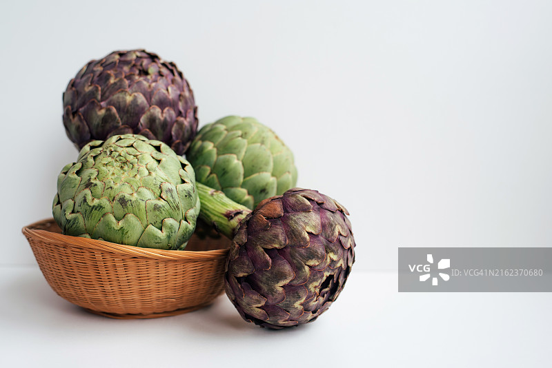 柳条筐里的绿色和紫色朝鲜蓟。异国情调的蔬菜。健康食品。农场收获。菜肴配料。图片素材