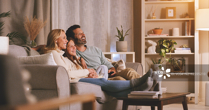 周末居家：父母和女儿在客厅沙发上看电视，享受电影和喜剧图片素材