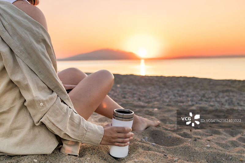 戴着草帽的女人坐在沙滩上，欣赏日出的背影。冥想图片素材