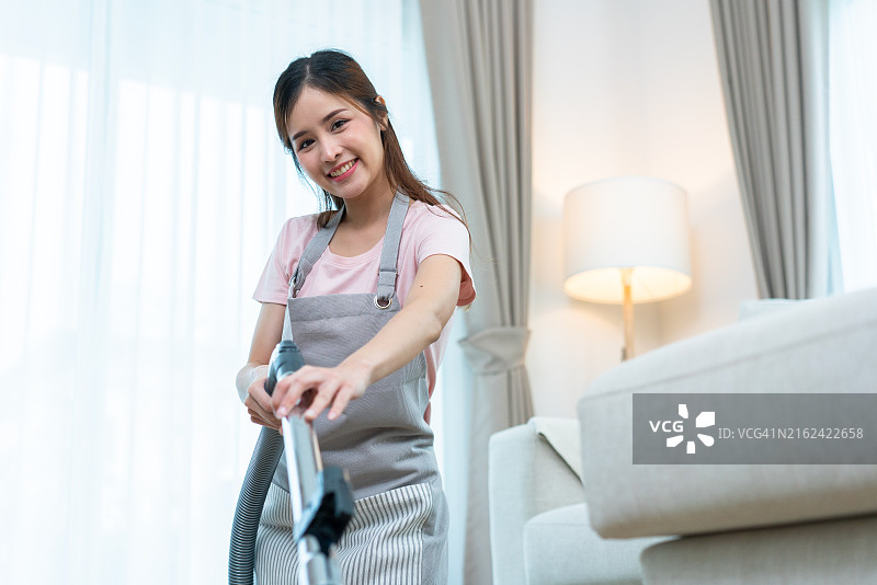 微笑着在客厅吸尘的女人图片素材