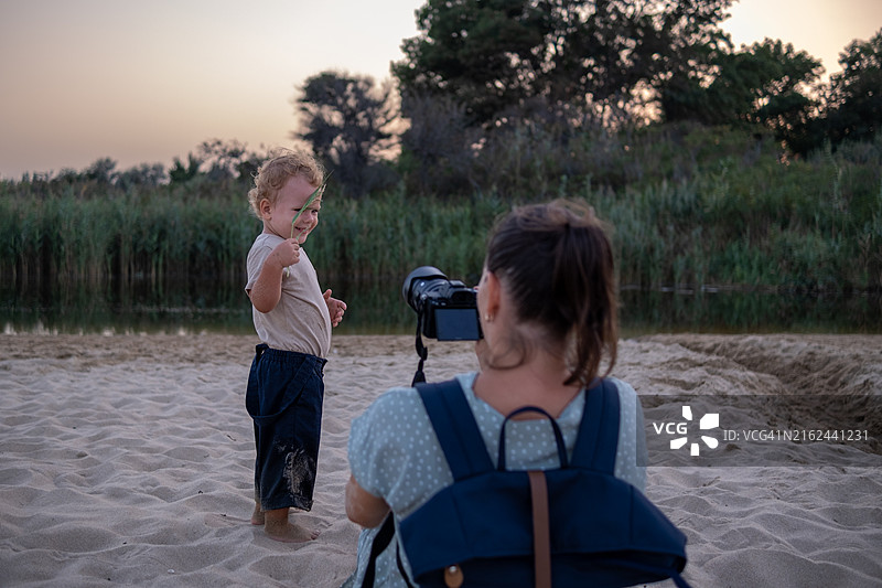 快乐的母亲在海滩上给儿子拍照，小溪流入大海，日落时分图片素材
