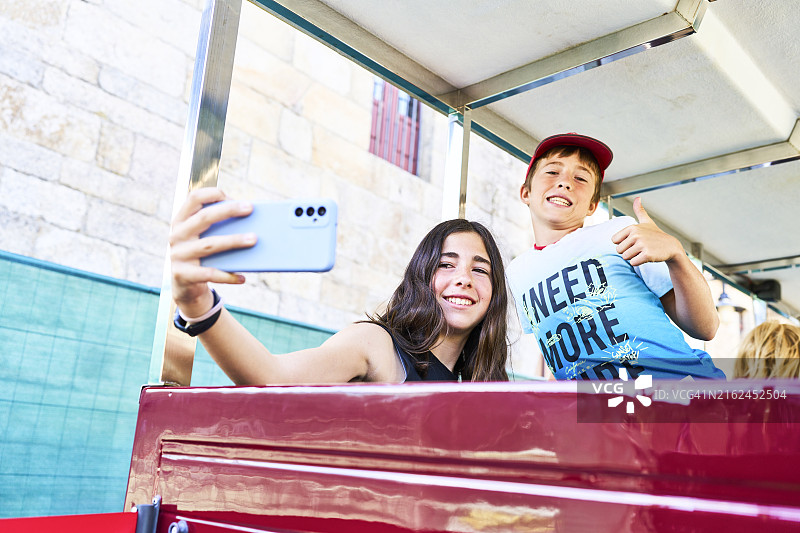 年轻女子与哥哥在长椅上用手机自拍图片素材