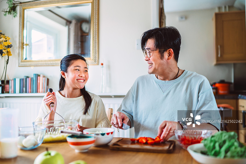 年轻的亚洲父亲和十几岁的女儿在厨房里一起愉快地准备饭菜图片素材