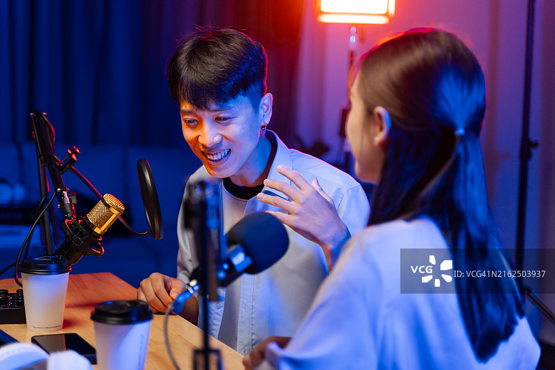 快乐的年轻男女播客在演播室进行日常直播，与粉丝互动，彩色灯光已设置图片素材