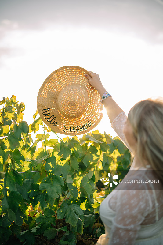 在葡萄园里散步的戴草帽女子背影图片素材