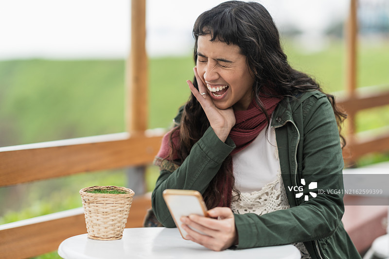 在餐厅等候时，一边看手机一边开怀大笑的女人图片素材