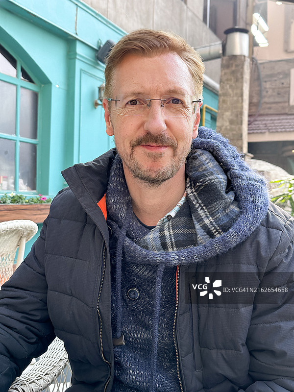 舒适的户外氛围：穿连帽衫的男人坐在寒冷天气下的咖啡馆或酒吧外图片素材