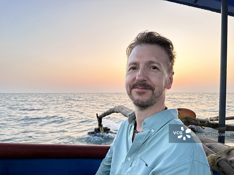 日落航行：戴太阳镜的男人在海滩船上放松身心图片素材