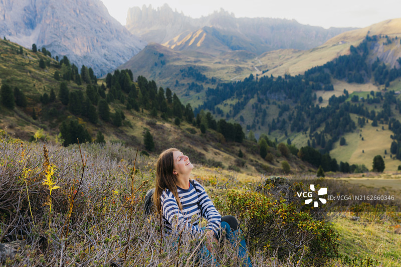 女人在风景优美的草地上放松，思考日落时分的美丽山脉图片素材