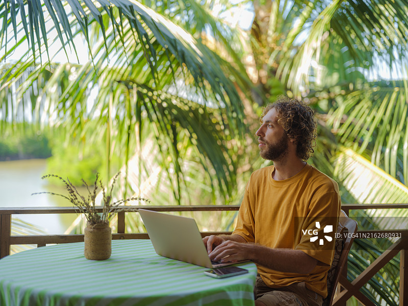 在棕榈树下露台上使用笔记本电脑的男人图片素材