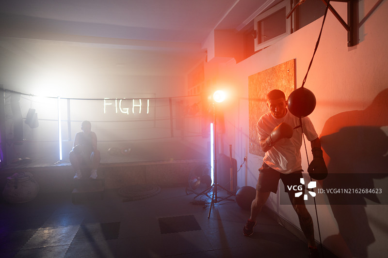 在霓虹灯闪烁的拳击俱乐部里打沙袋的英俊男拳击手图片素材