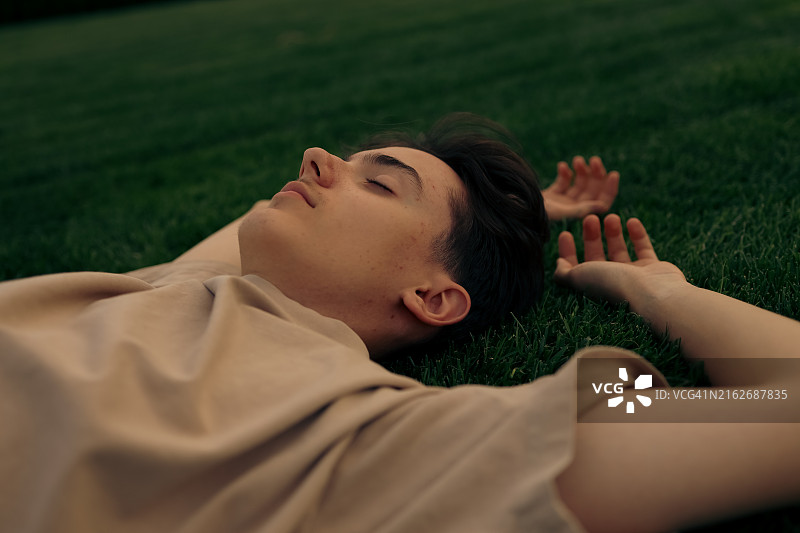 年轻男孩闭着眼睛在草地上放松图片素材