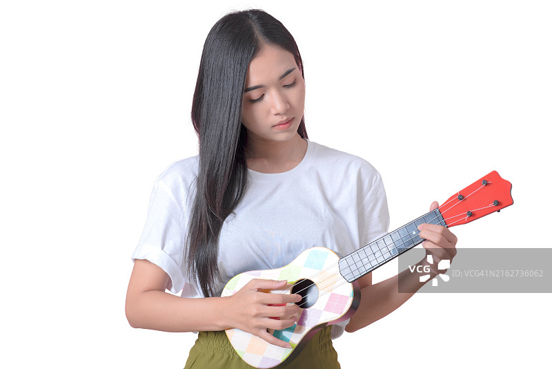 手持尤克里里的快乐女孩站在白色背景上，微笑的女孩音乐家弹奏尤克里里，已隔离图片素材