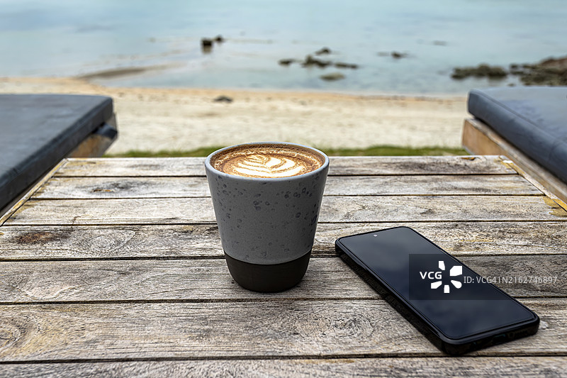 海滩边的木桌上的陶瓷杯卡布奇诺图片素材