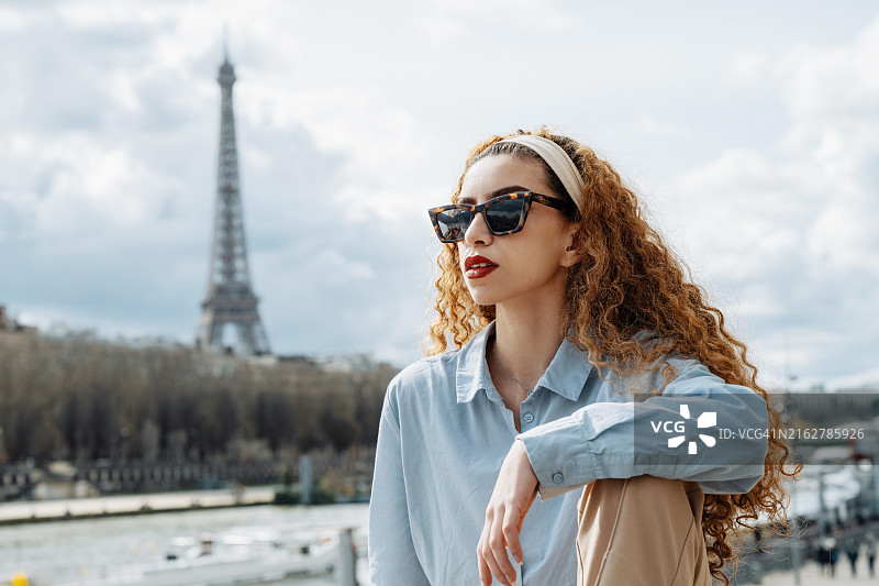 时尚千禧一代女性戴着太阳镜站在阴天下的埃菲尔铁塔前图片素材