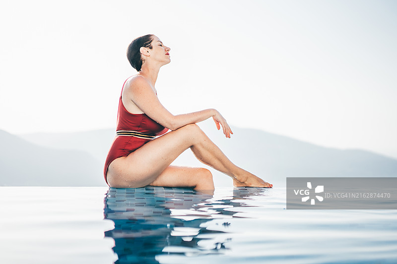 女人在日落时分享受无边泳池的魔幻景色。图片素材