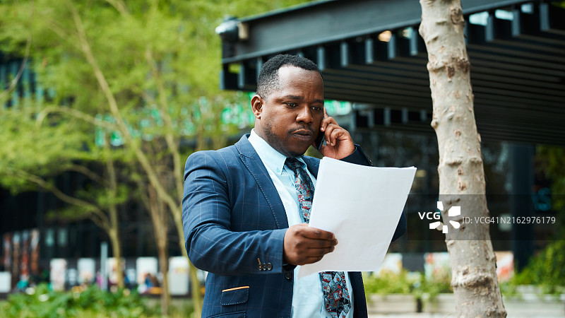 在城市公园通过电话阅读文件的非裔美国商人图片素材