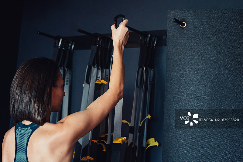 在健身房用TRX健身带训练手臂的女人图片素材