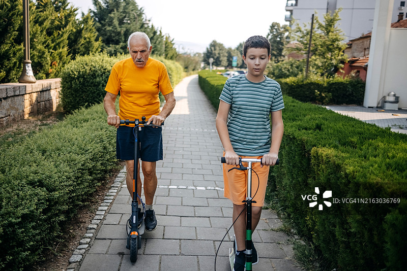 年长的男人和孙子一起在城市里骑电动滑板车图片素材