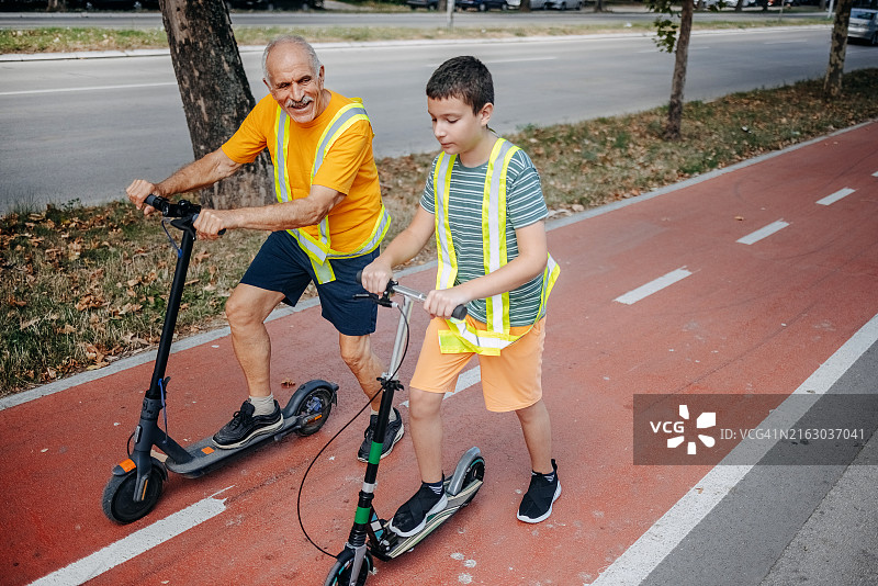 年长的男人和孙子一起在城市里骑电动滑板车图片素材