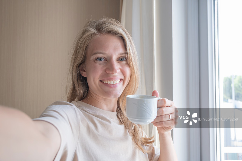 居家窗边手持咖啡杯的微笑女人肖像图片素材
