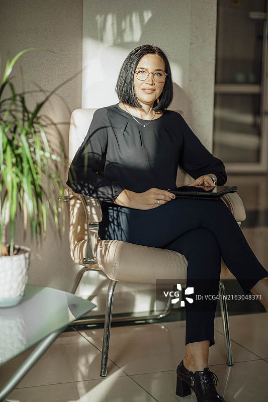 工作与生活平衡：商务女性坐在大厅的椅子上使用平板电脑图片素材