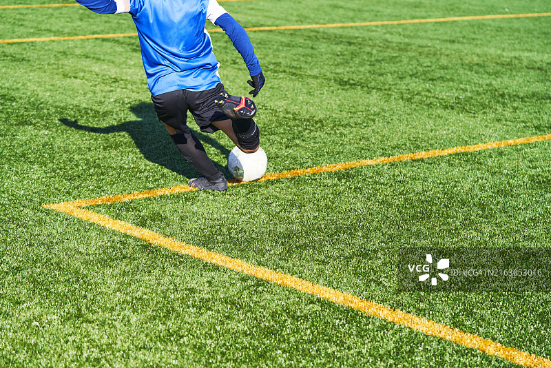 草地上，身穿蓝色制服的男孩踢足球的背影图片素材