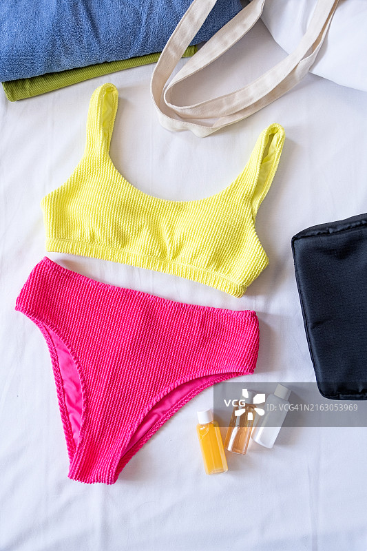 旅行化妆品套装和泳衣在床上，顶视图图片素材