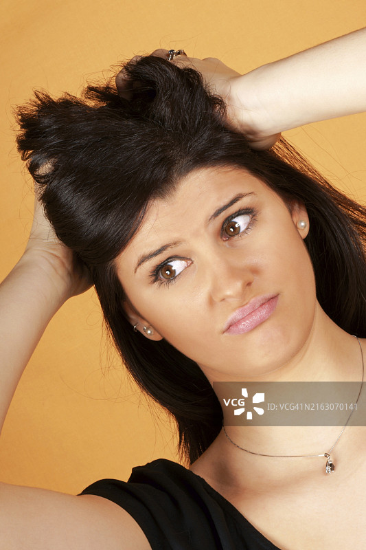 一个忧心忡忡的18岁年轻女子在橙色背景上的肖像图片素材