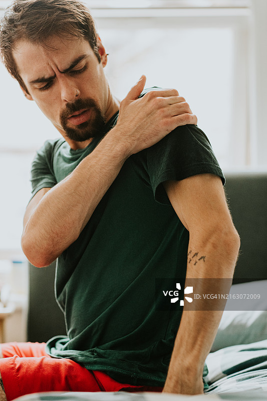 男人醒来时捂住疼痛的肩膀，在床上畏缩图片素材
