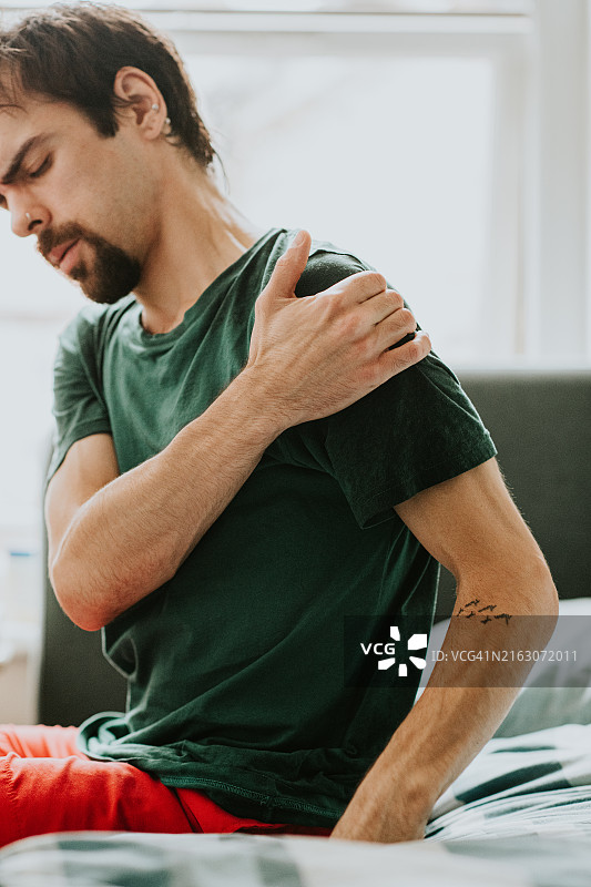 男人醒来时捂住疼痛的肩膀，在床上畏缩图片素材