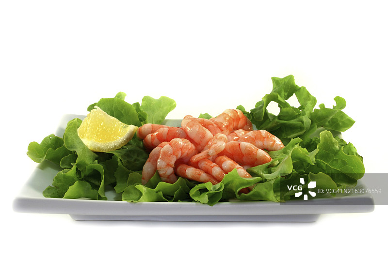 盘中铺满生虾和柠檬的生菜叶图片素材