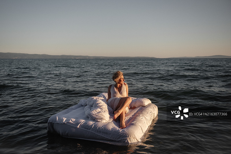 在日落时分海洋中的漂浮床上微笑的女人图片素材