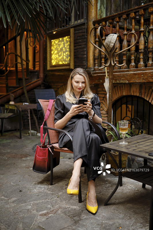 时尚女人在酒吧露台上用手机给朋友发信息，说正在等他们图片素材