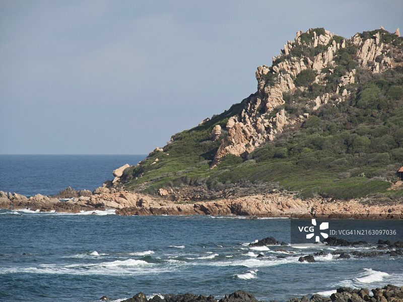 蓝色天空下，科西嘉阿雅克肖的岩石峭壁与海浪图片素材