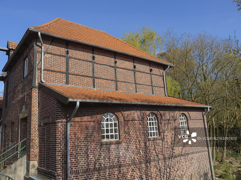 德国威斯特法伦州梅特伦，晴朗的春日里，一栋有着小窗户和红色屋顶的古老砖砌建筑，周围环绕着光秃秃的树木图片素材