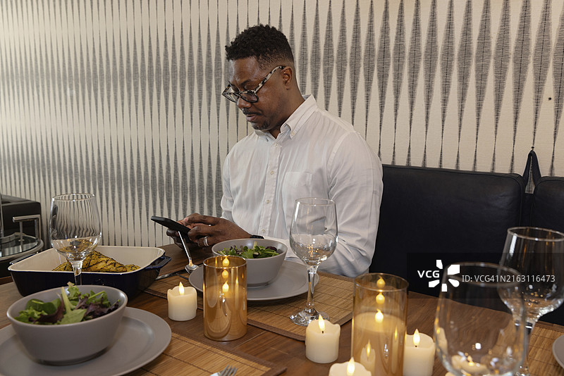 成熟男性在餐桌上用智能手机享用晚餐图片素材
