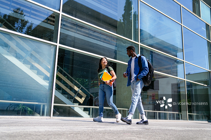大学生背着书包和笔记本在校园里行走图片素材