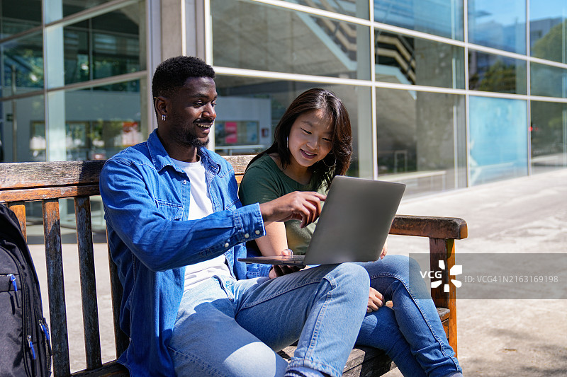 两名大学生在校园长椅上使用笔记本电脑图片素材