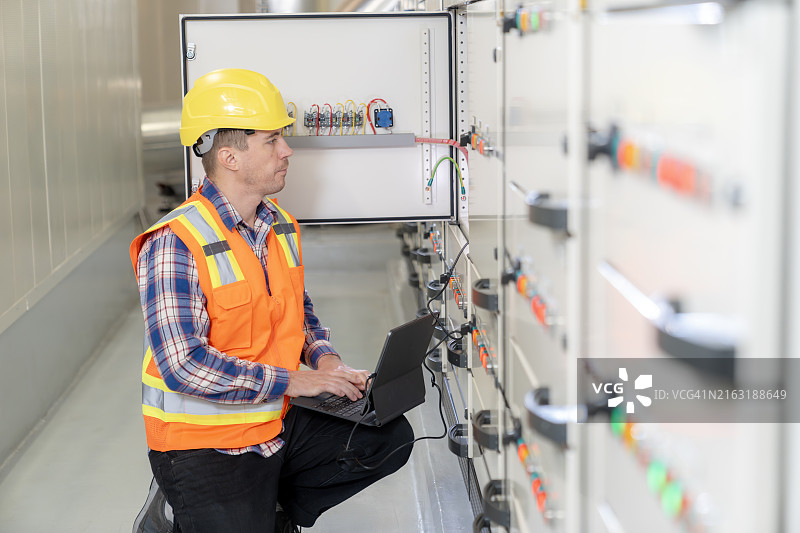 一名男电气工程师正在使用笔记本电脑检查建筑物电气控制系统的运行情况图片素材
