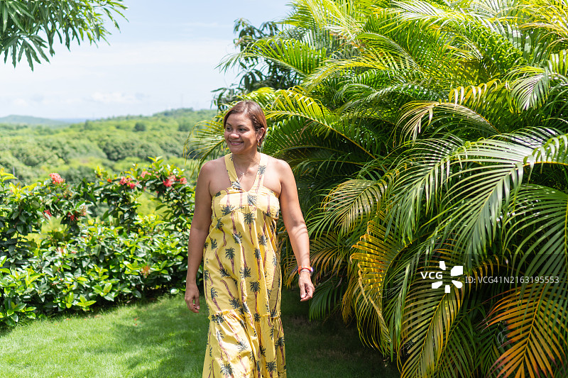 穿着黄色热带连衣裙欣赏花园景色的拉丁女人图片素材