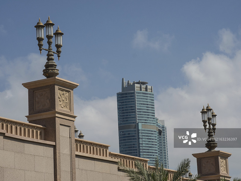 阿联酋阿布扎比的蓝天下，以装饰灯笼和石墙为前景的摩天大楼图片素材