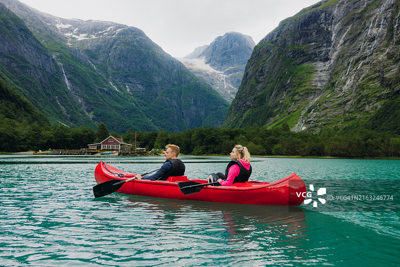 快乐的夫妇划着红色独木舟穿越水晶般的蓝色湖面，欣赏冰川景色图片素材