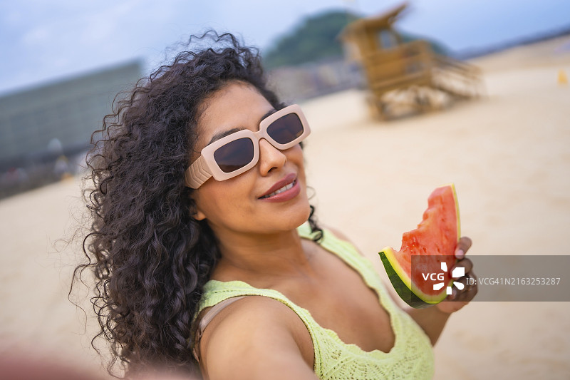 拉丁裔女子在海滩度假，手拿西瓜自拍图片素材