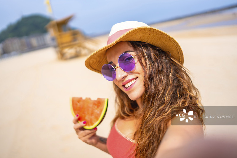 白人女性在海滩度假享受夏日，戴着帽子和西瓜的自拍图片素材