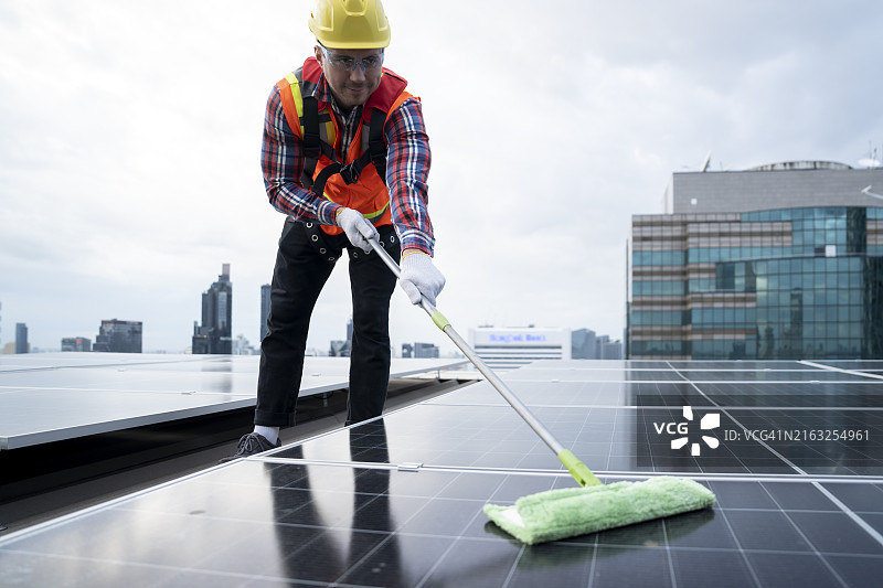 男工程师在高楼顶上清洁光伏板系统。图片素材