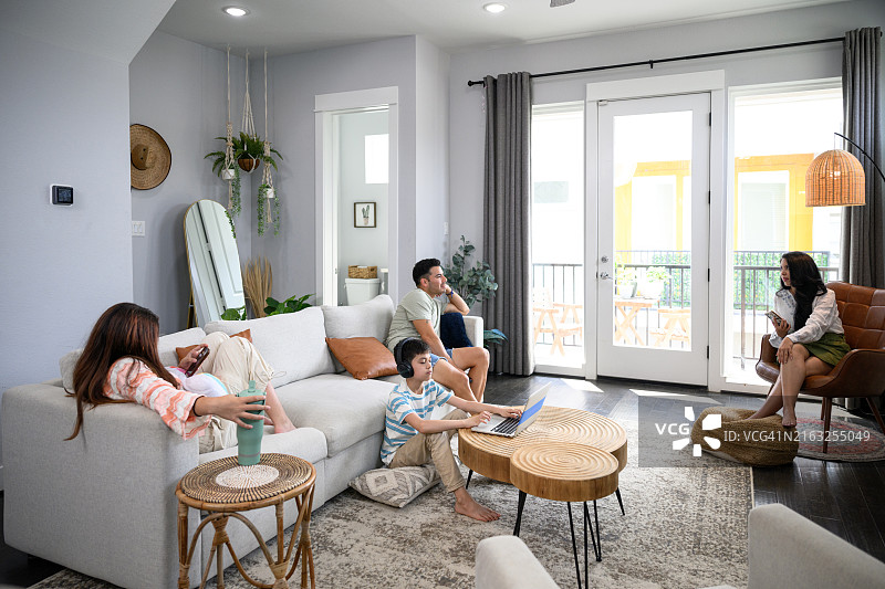 在公寓客厅里使用电子设备的现代拉丁美洲家庭的广角景观图片素材